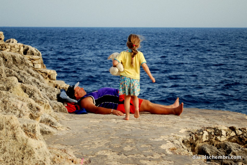 A girl approaches her father, who is trying to sunbathe. © All rights reserved David Schembri 2010